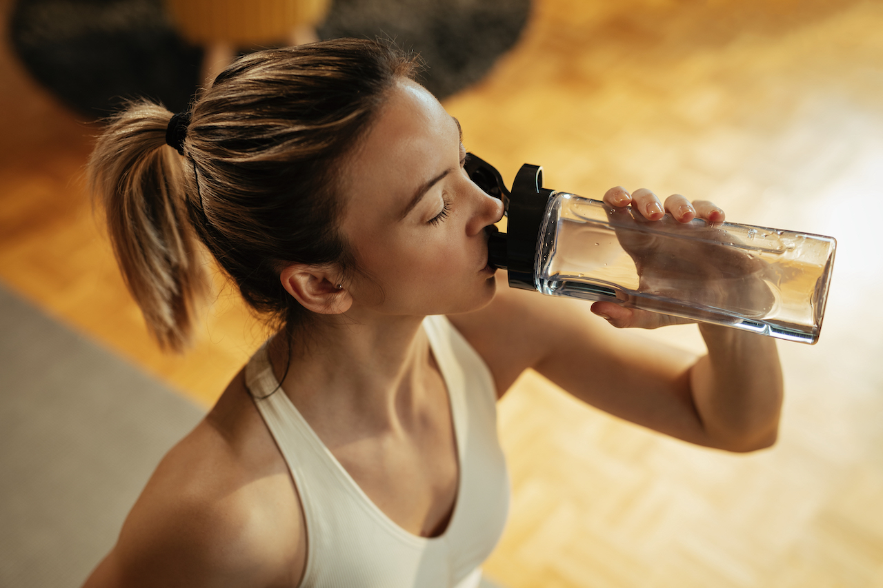 Above view of thirsty sportswoman drinking water.